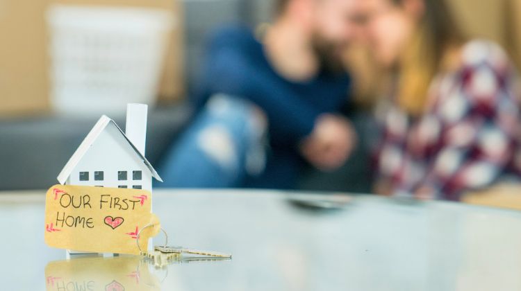 couple blurred out in background, focus on toy home with a sign that says our first home