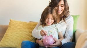mother sitting on couch with small child adding money to a piggy bank