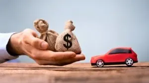 hand holding bags of money in front of a toy car