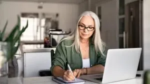 woman sitting at a table in her kitchen researching mortgage payment savings from a refinance